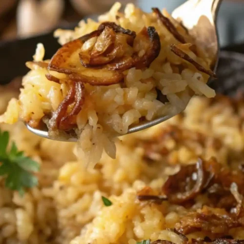 Close-up of French onion butter rice topped with caramelized onions, served on a spoon with fresh parsley garnish in the background.