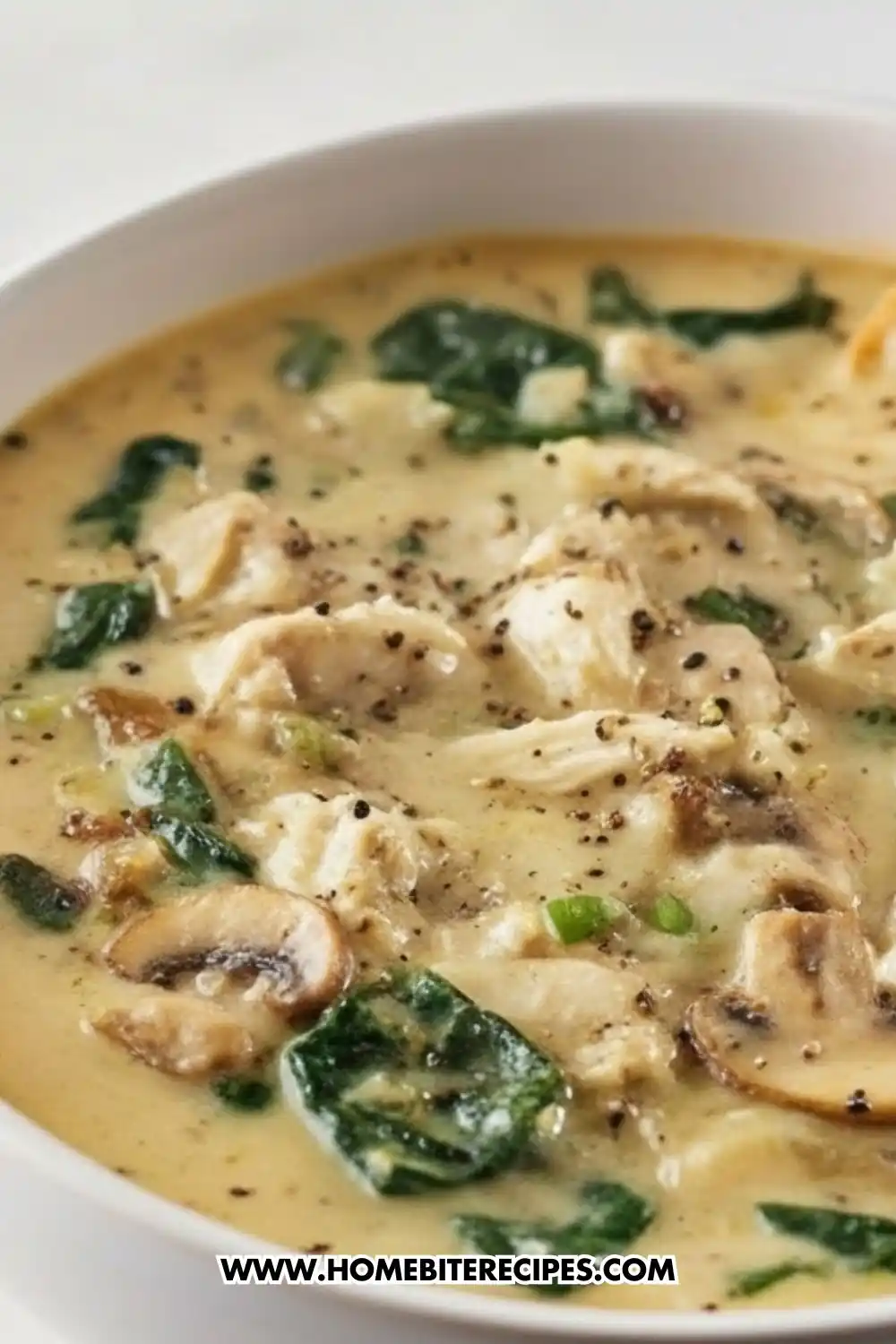 Creamy rotisserie chicken mushroom soup with spinach, served in a white bowl and seasoned with black pepper.