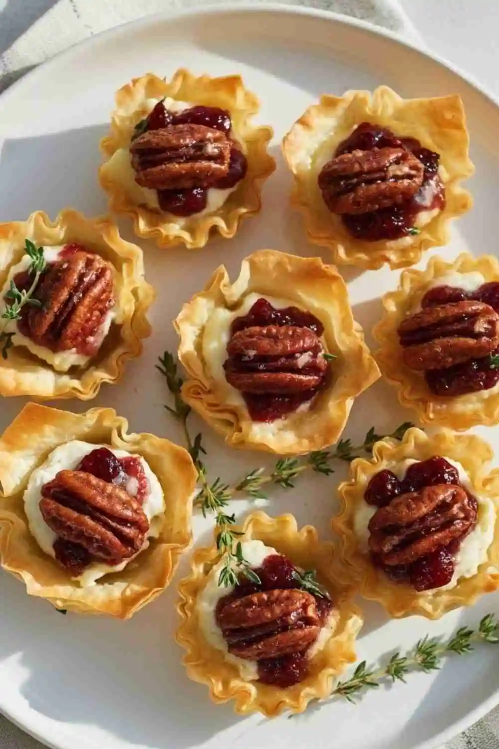 Candied pecan and cranberry brie bites in crispy phyllo cups with fresh thyme.