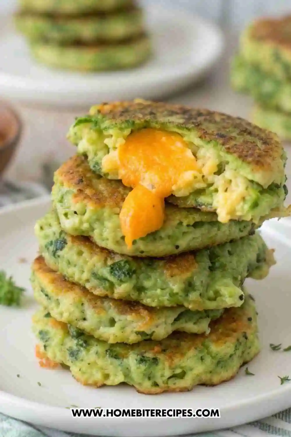 Stack of crispy cheesy broccoli fritters with melted cheddar cheese oozing out, served on a white plate.