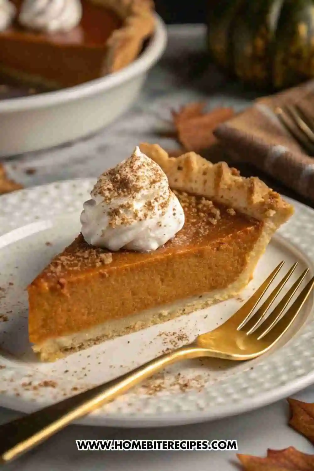 Slice of Classic Homemade Pumpkin Pie with whipped cream and cinnamon on top, served on a white plate with a gold fork.