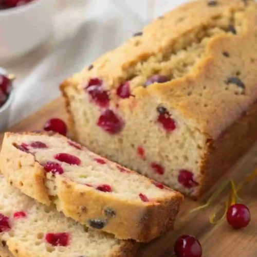 Moist cranberry orange bread loaf with fresh cranberries and orange zest slices on a wooden board.