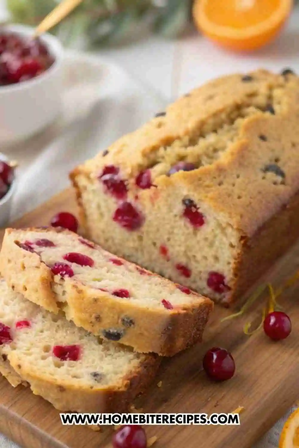 Moist cranberry orange bread loaf with fresh cranberries and orange zest slices on a wooden board.