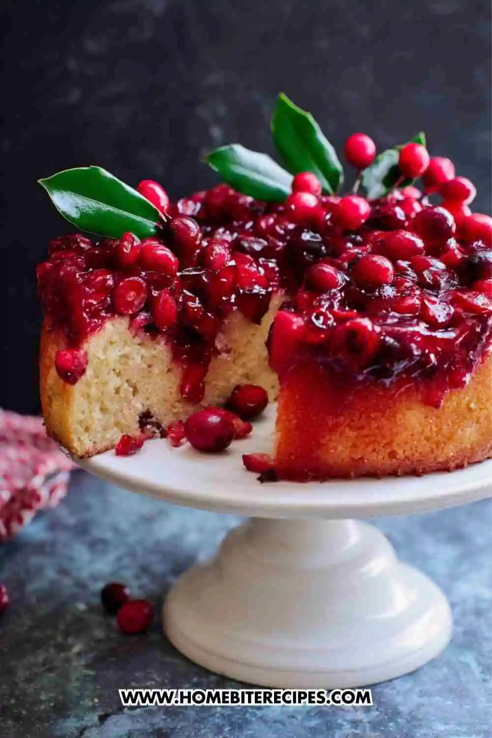 Moist cranberry upside-down cake topped with glossy caramelized cranberries on a white cake stand.