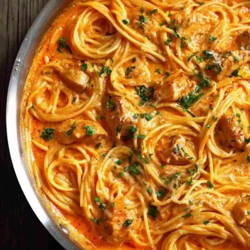 creamy garlic chicken pasta coated in a rich tomato-cream sauce, garnished with fresh parsley.