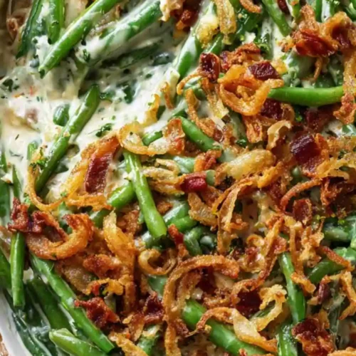 Creamy green bean casserole topped with crispy fried onions and bacon pieces.
