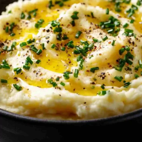 Smooth and creamy mashed potatoes topped with melted butter, freshly cracked black pepper, and chopped chives in a black bowl.