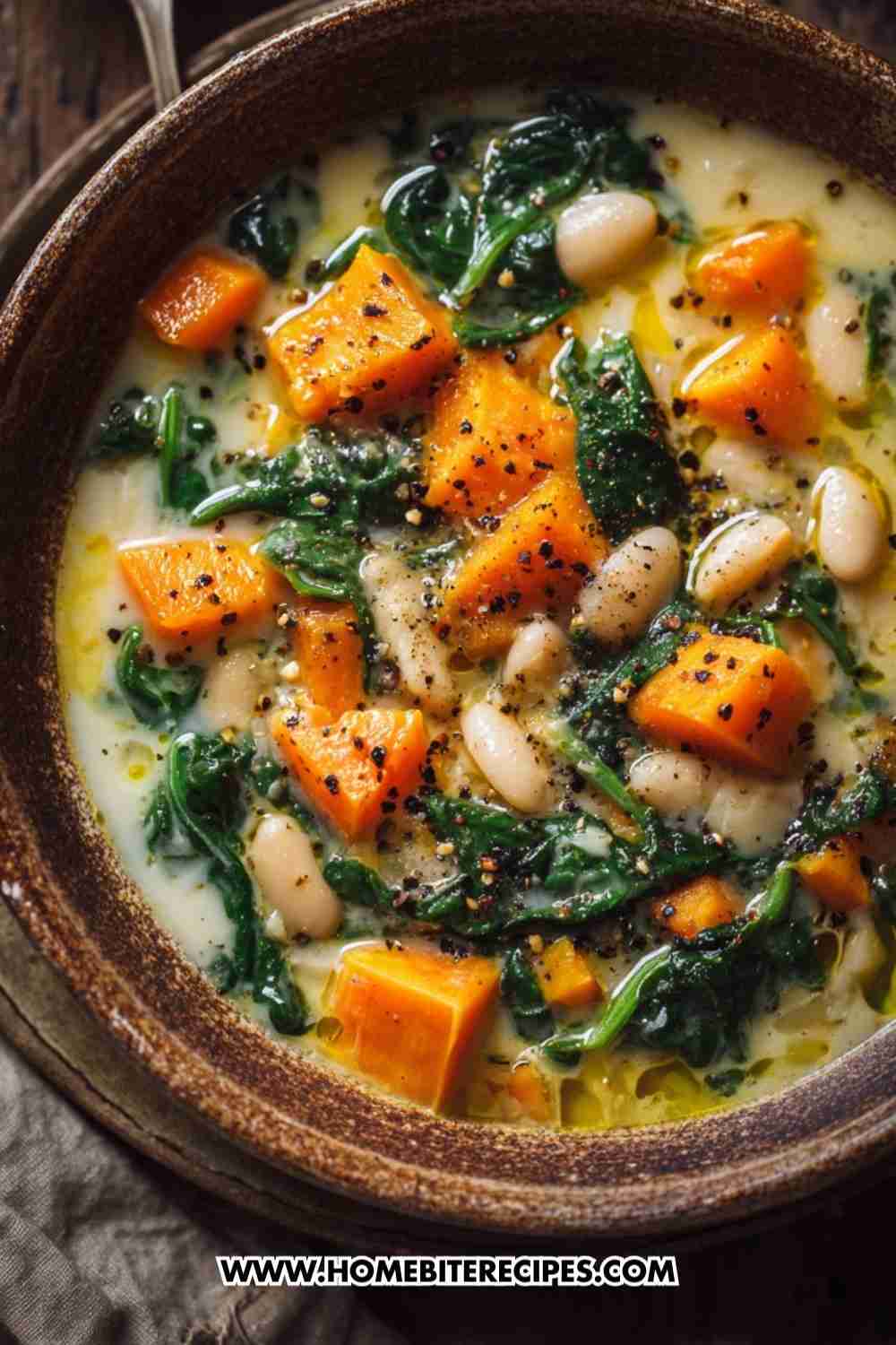 A bowl of creamy pumpkin soup with white beans, spinach, and black pepper, drizzled with olive oil — a cozy vegan and gluten-free fall meal.