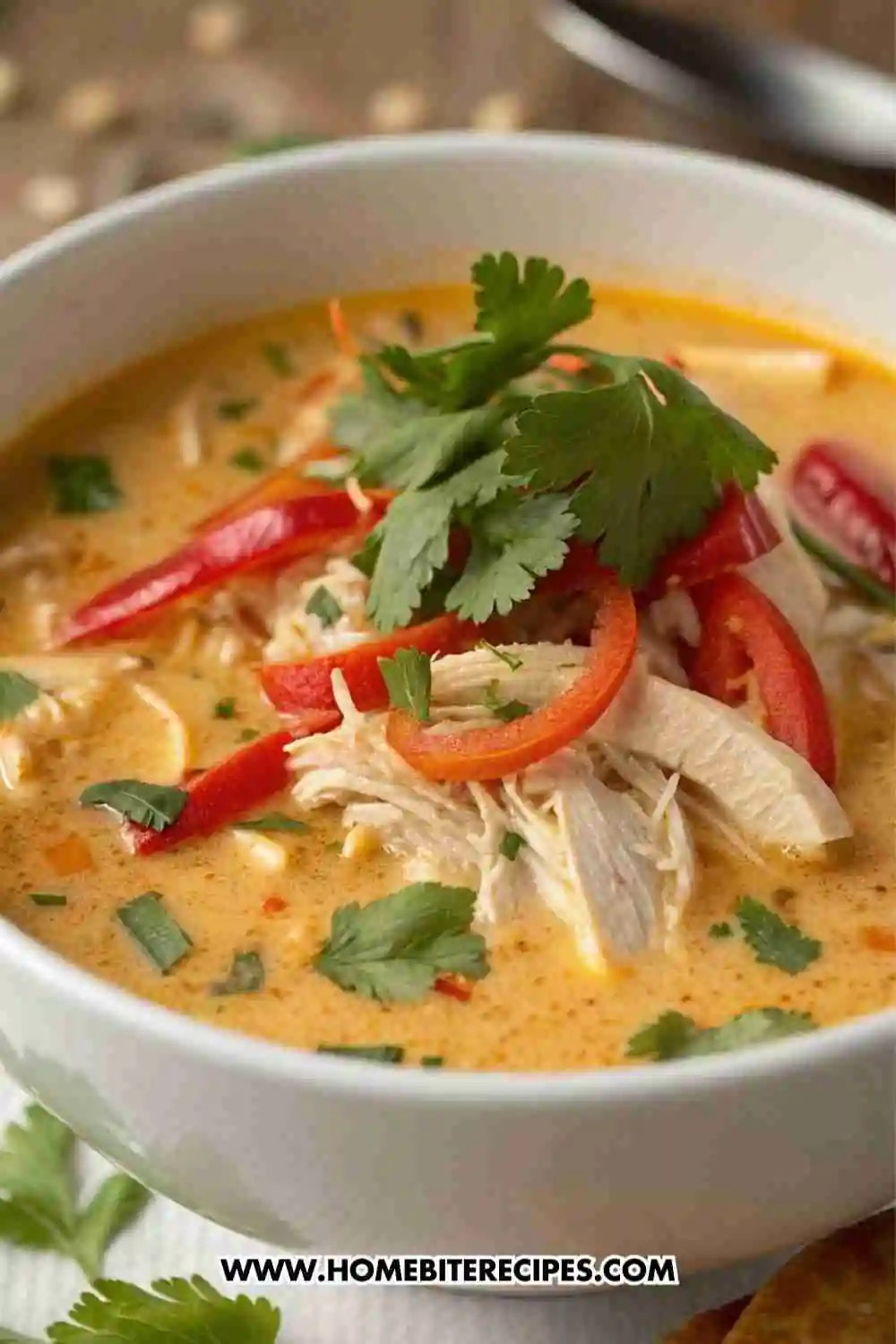 A bowl of creamy Thai coconut chicken soup topped with red peppers, cilantro, and shredded chicken in a rich coconut broth.