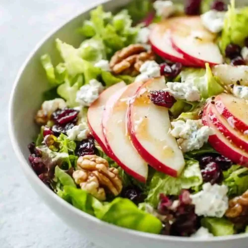 Fresh apple walnut salad with blue cheese, dried cranberries, and honey dressing in a white bowl.