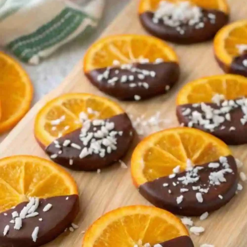 Dark chocolate dipped orange slices topped with shredded coconut on a wooden board.