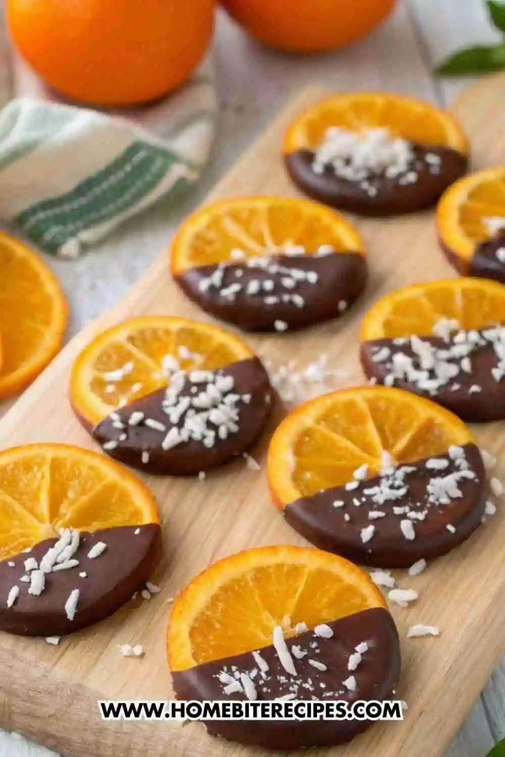 Dark chocolate dipped orange slices topped with shredded coconut on a wooden board.