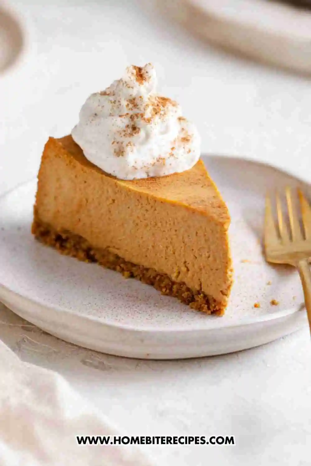 Slice of creamy baked pumpkin cheesecake with a gingersnap crust, topped with whipped cream and cinnamon on a white plate.