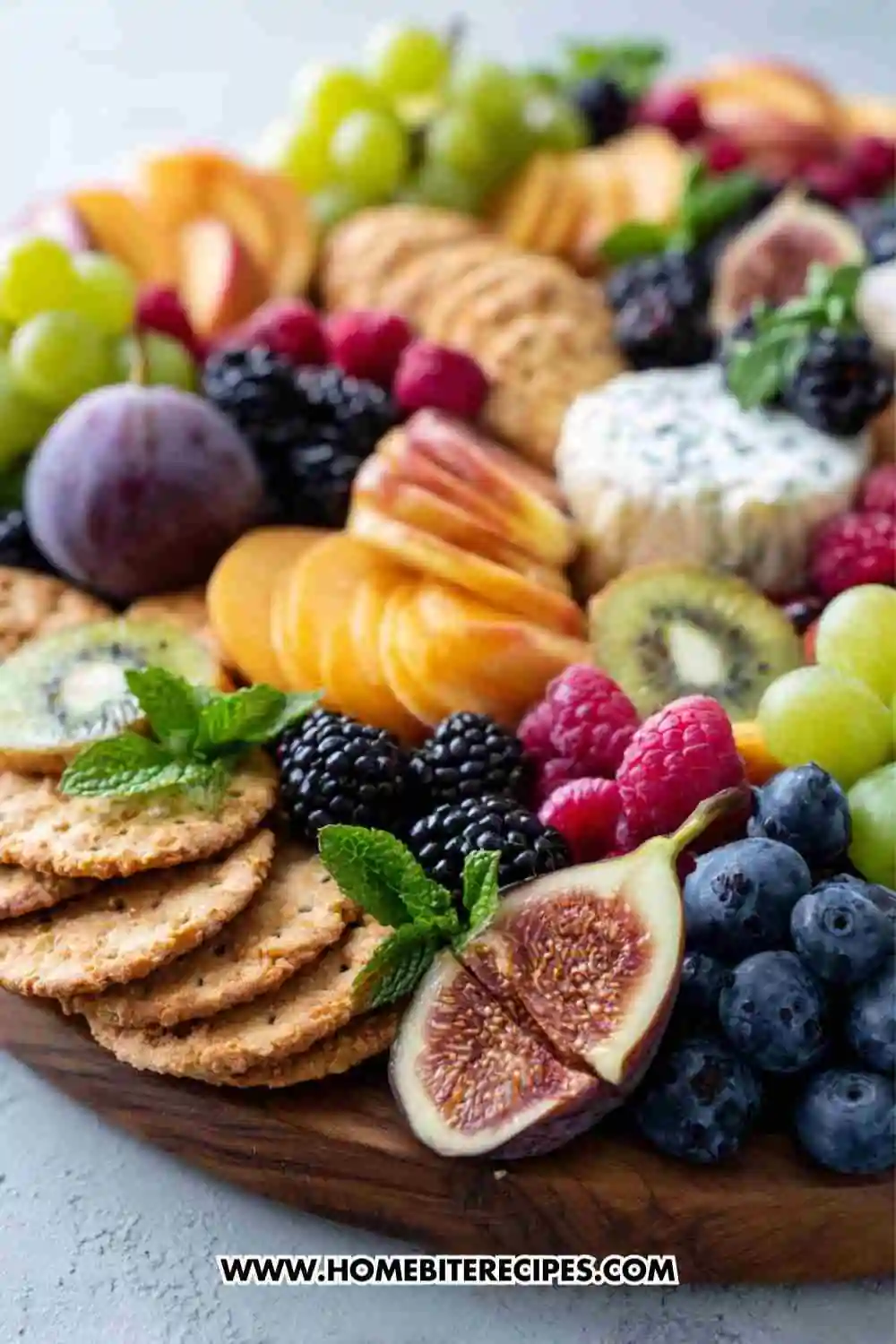 Colorful fruit and cheese board featuring grapes, figs, berries, kiwi, crackers, and assorted cheeses arranged beautifully on a wooden platter.