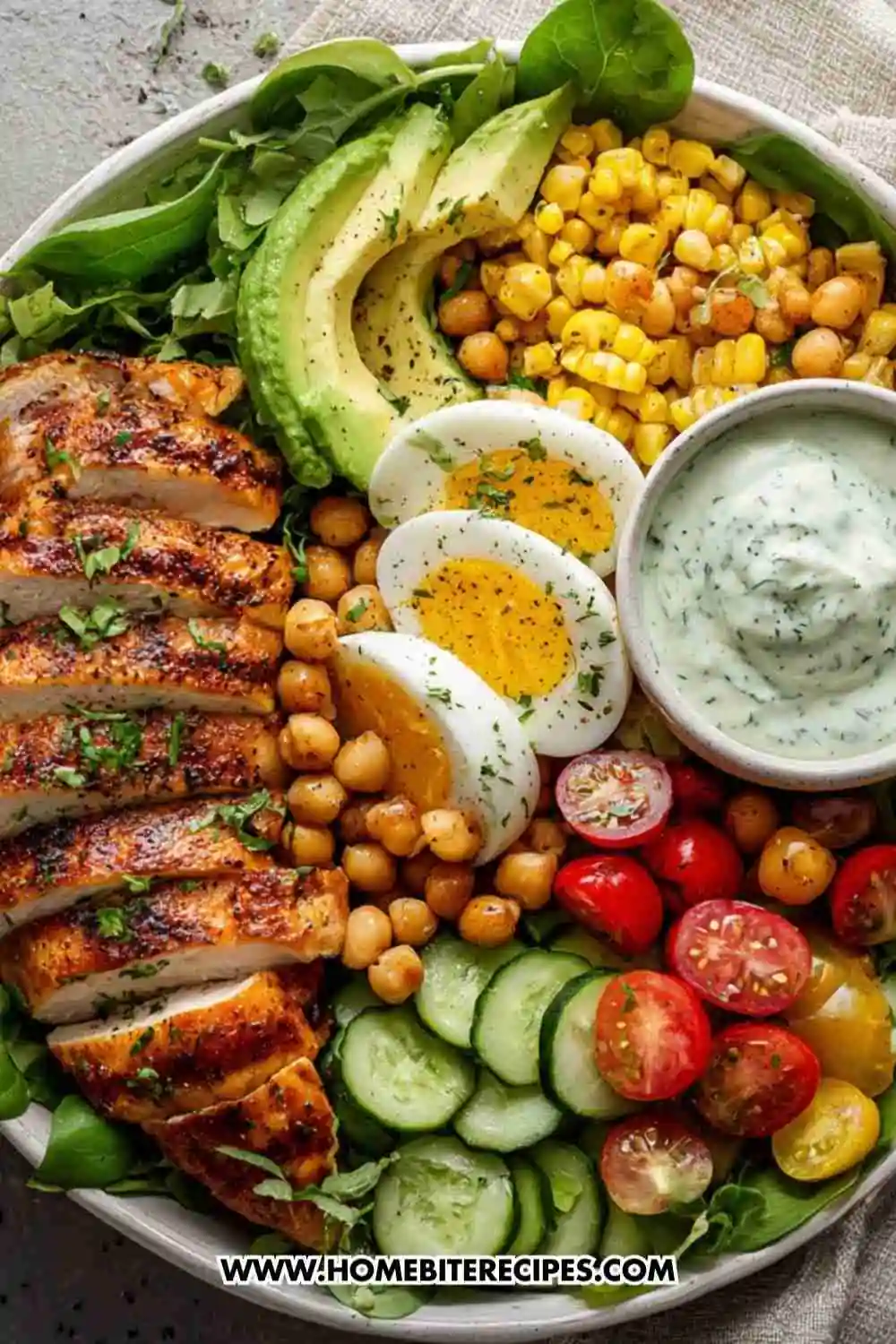 Grilled chicken power bowl with avocado, chickpeas, hard-boiled eggs, corn, cucumbers, tomatoes, and herb dressing.