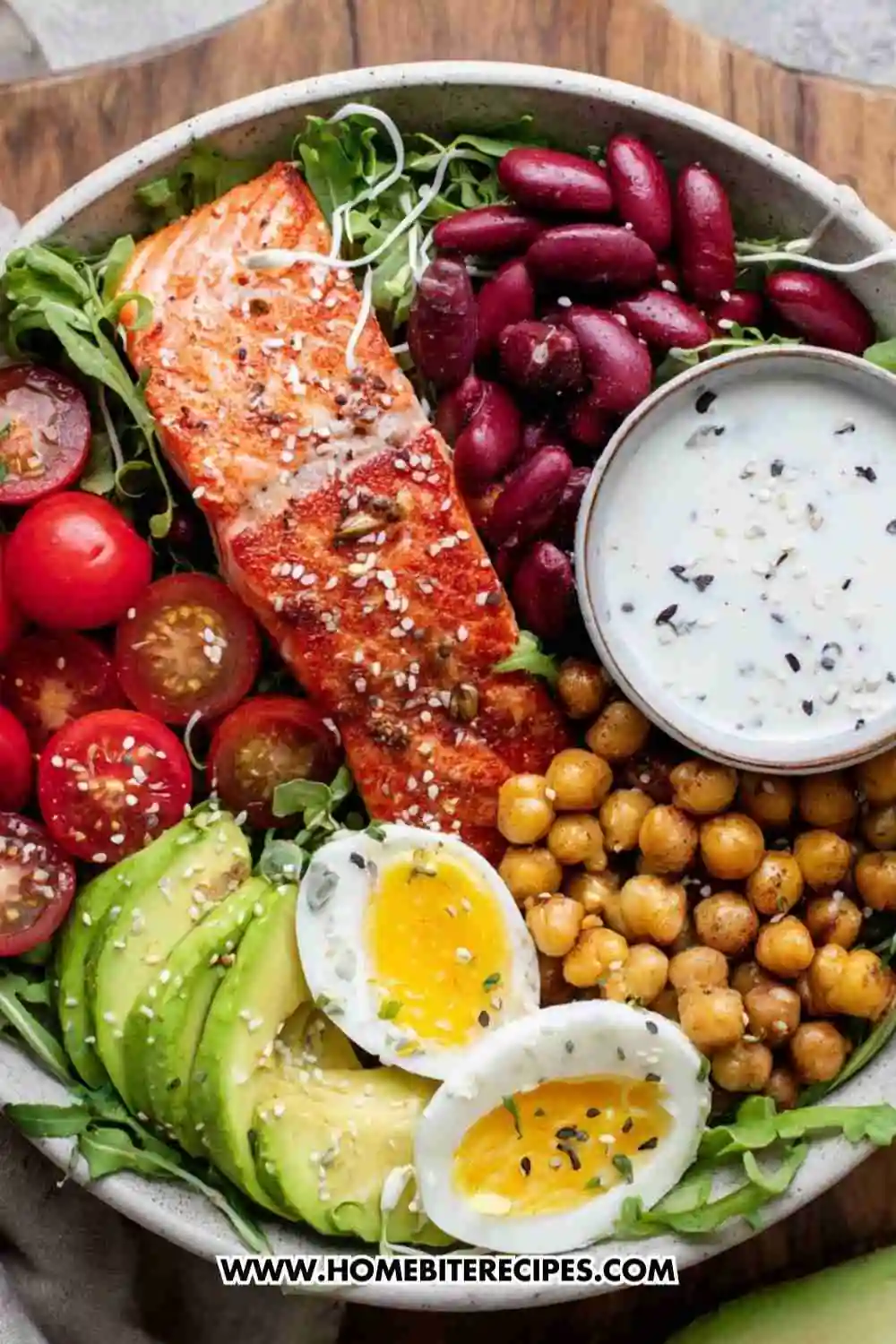 A vibrant salmon power bowl with grilled salmon, avocado, chickpeas, kidney beans, cherry tomatoes, soft-boiled egg, and yogurt dressing.