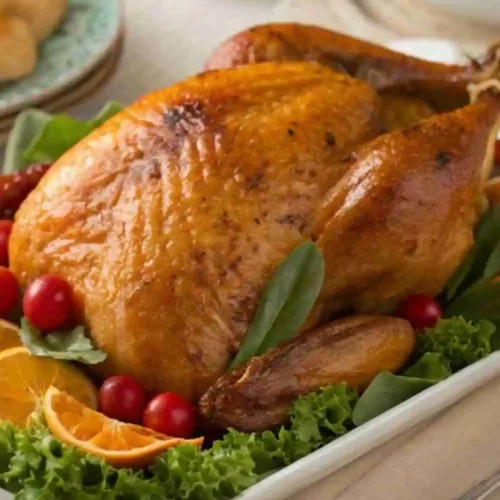Golden brown herb-roasted whole chicken garnished with fresh greens, orange slices, and cherry tomatoes.
