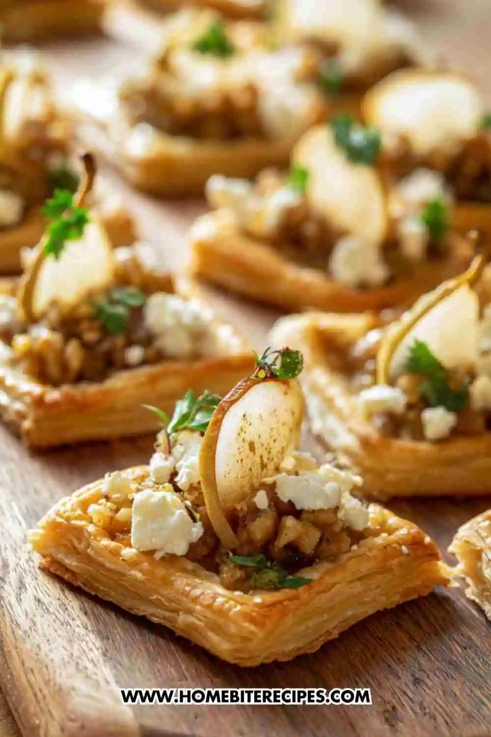 Mini puff pastry bites topped with caramelized pear slices, creamy goat cheese, walnuts, and herbs on a wooden board.