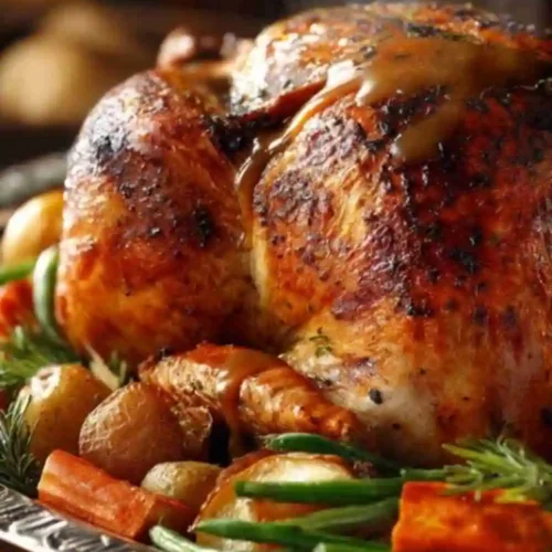 Golden Perfect Juicy Thanksgiving Roast Turkey Recipe topped with gravy, surrounded by roasted carrots, potatoes, and herbs on a serving platter.