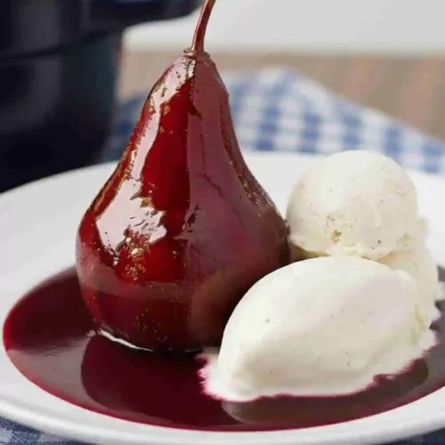 Poached Pears with Cinnamon and Pomegranate Syrup served with vanilla ice cream on a white plate, set on a checkered cloth background.
