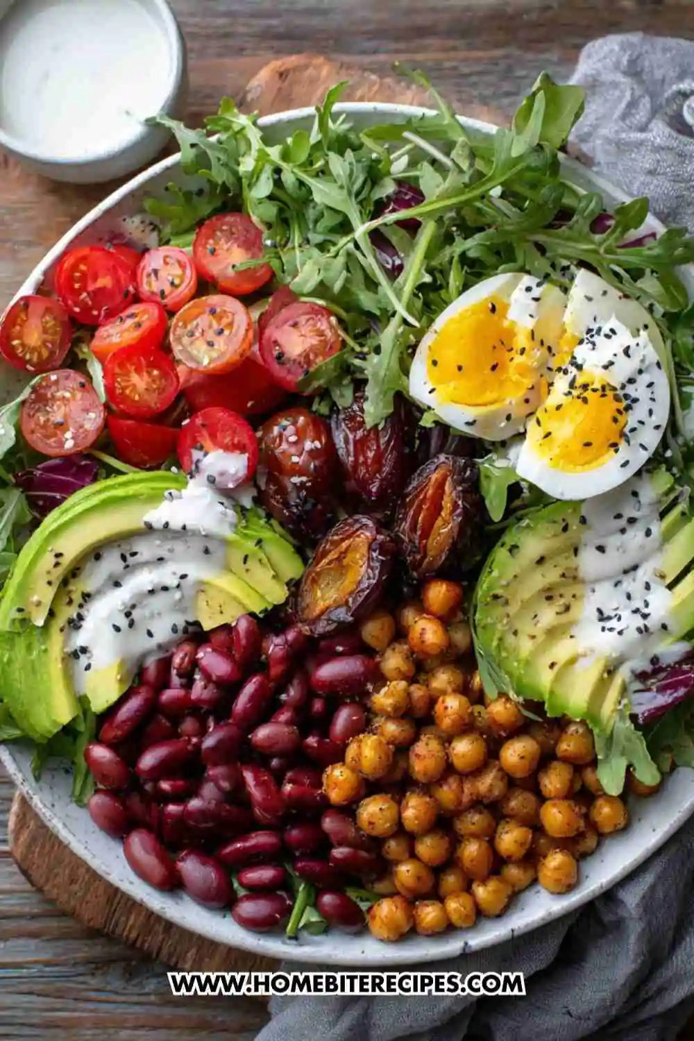 Colorful salad bowl with crispy chickpeas, avocado slices, boiled eggs, cherry tomatoes, dates, red beans, and yogurt dressing on arugula greens.