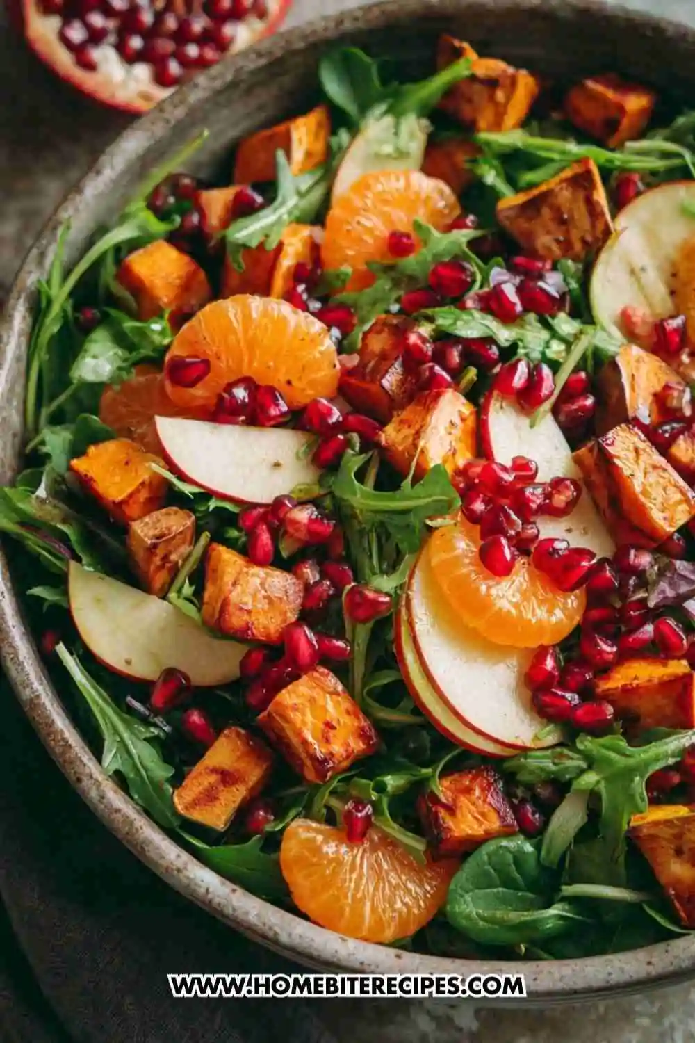 A vibrant salad with roasted sweet potatoes, arugula, pomegranate seeds, mandarin slices, and apple tossed in citrus vinaigrette.