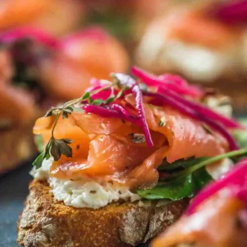 Crispy crostini topped with cream cheese, smoked salmon, fresh herbs, and pickled onions — elegant appetizer presentation.