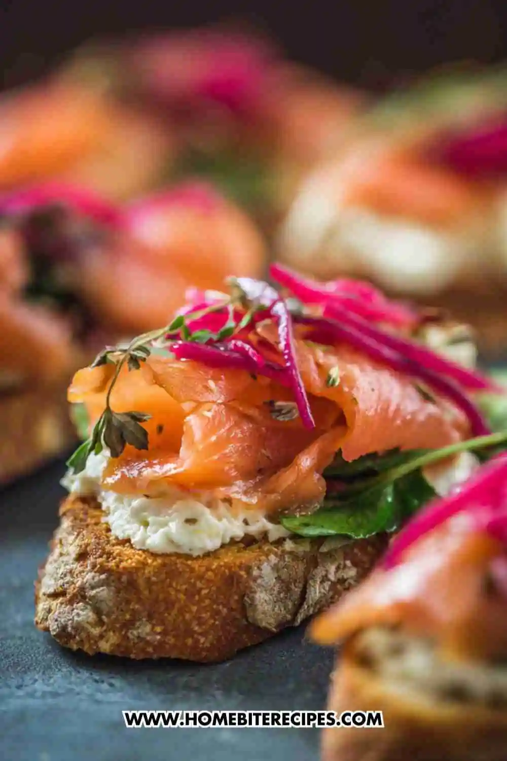 Crispy crostini topped with cream cheese, smoked salmon, fresh herbs, and pickled onions — elegant appetizer presentation.