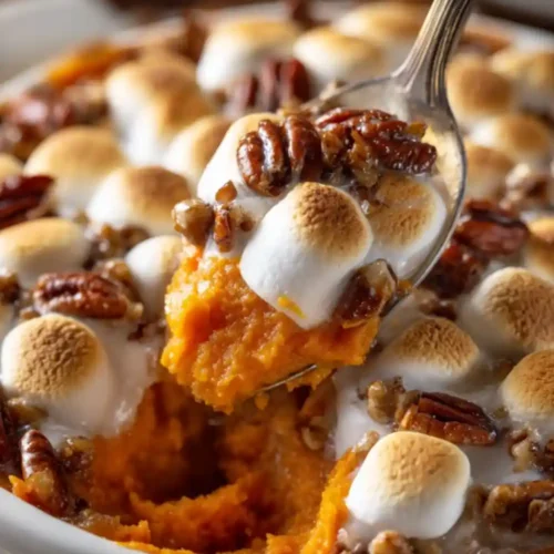 A close-up of homemade sweet potato casserole topped with toasted marshmallows and pecans in a white baking dish — a classic Thanksgiving dessert or side dish.