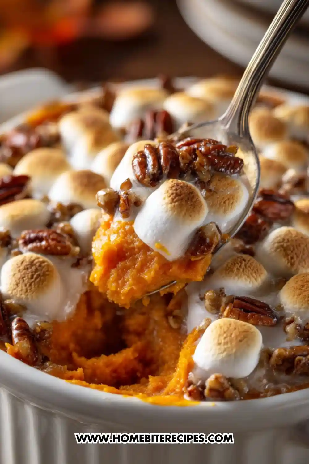 A close-up of homemade sweet potato casserole topped with toasted marshmallows and pecans in a white baking dish — a classic Thanksgiving dessert or side dish.