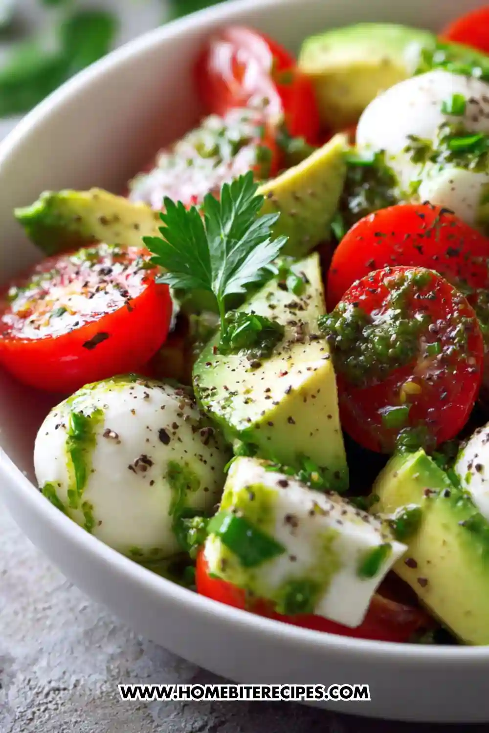 Colorful bowl of Avocado Caprese Salad with Fresh Pesto Dressing made with cherry tomatoes, mozzarella balls, avocado slices, and pesto dressing, garnished with fresh parsley.