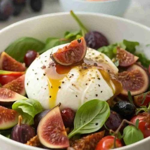 Creamy burrata salad with fresh figs, cherry tomatoes, arugula, and a honey balsamic glaze, garnished with basil and black pepper.