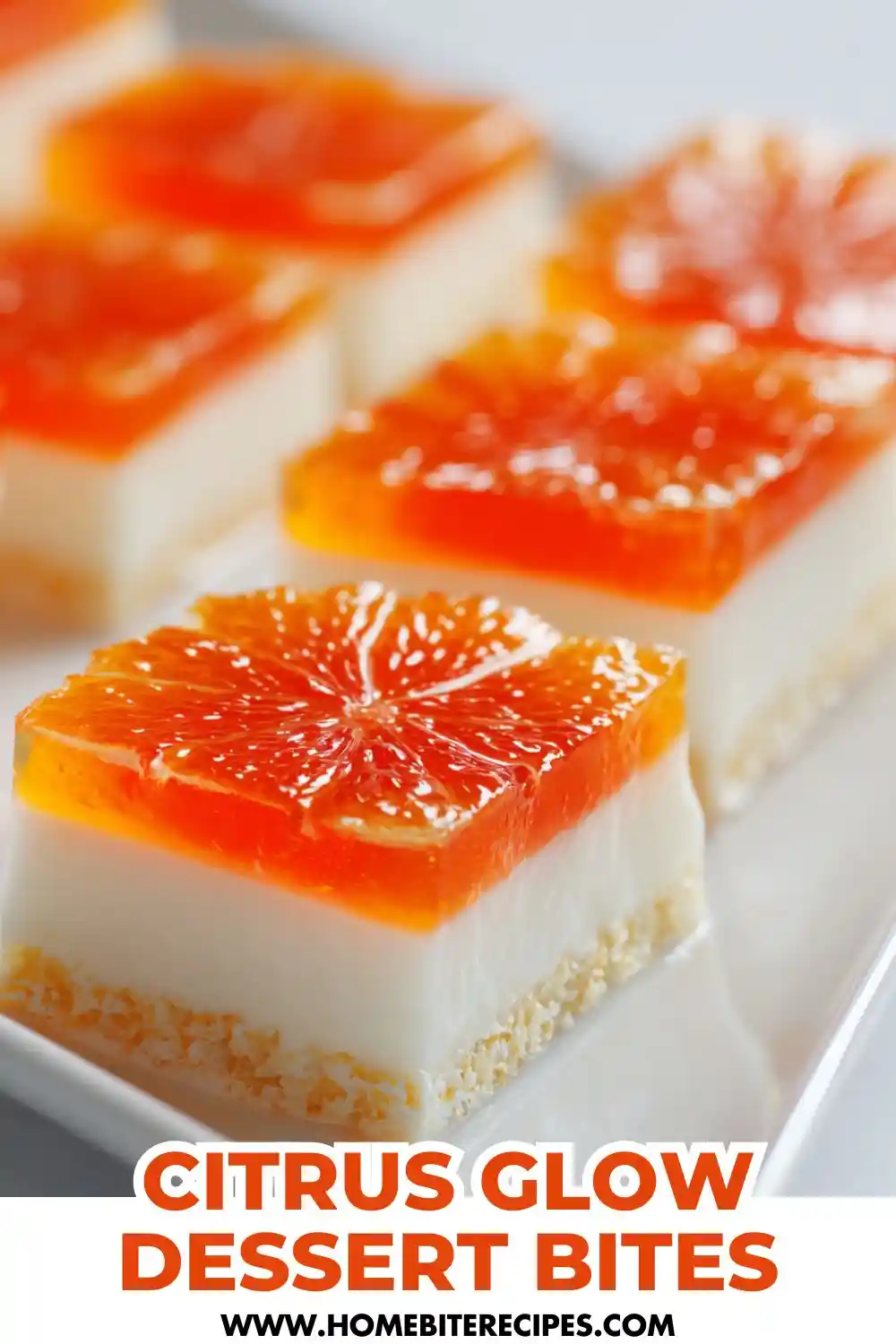 A close-up of layered citrus dessert bites featuring a bright orange gelatin top with citrus slices, creamy white middle layer, and a crumbly biscuit base, served neatly on a white platter.