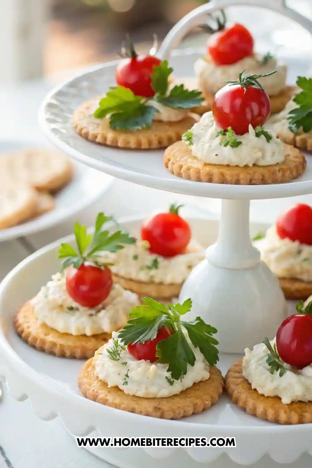Round crackers topped with creamy cheese spread, cherry tomatoes, and fresh parsley, served on a white tiered tray.
