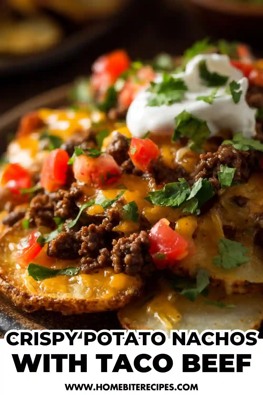 Close-up of crispy potato nachos topped with melted cheese, taco-seasoned ground beef, diced tomatoes, cilantro, and sour cream.