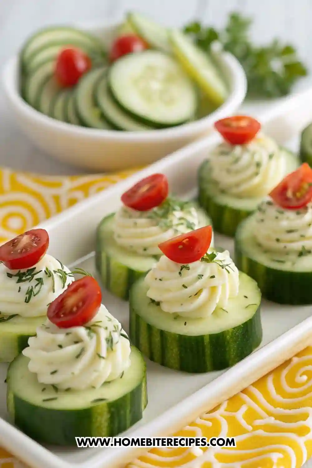 Cucumber rounds topped with piped herbed cream cheese and cherry tomato halves, served on a white platter — a light and refreshing party appetizer.