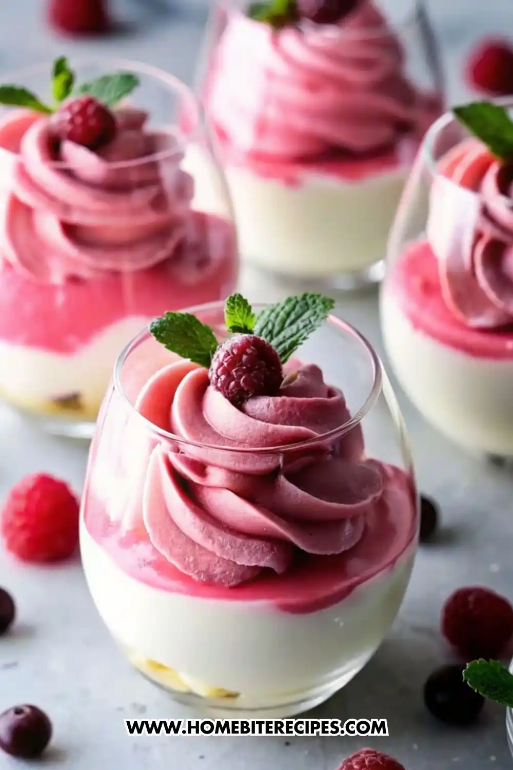 Glass cups filled with creamy layered cranberry mousse and vanilla cream, topped with a swirl of pink cranberry mousse, fresh cranberries, and mint leaves.