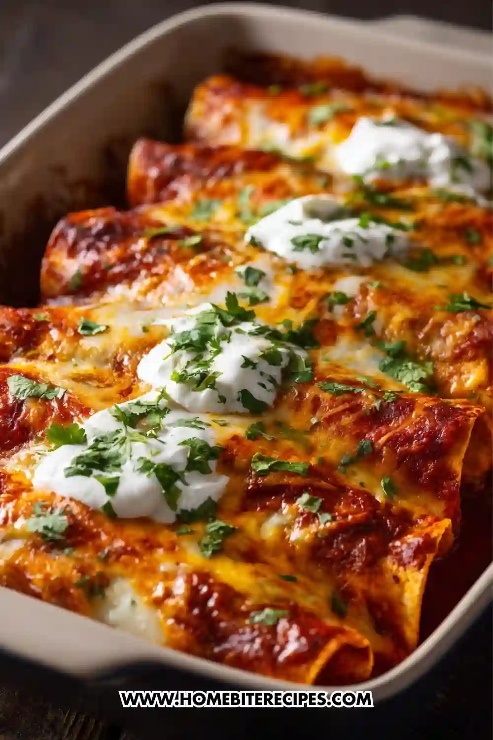 Close-up image of cheesy chicken enchiladas baked in a casserole dish, topped with melted cheese, red enchilada sauce, dollops of sour cream, and fresh chopped cilantro.
