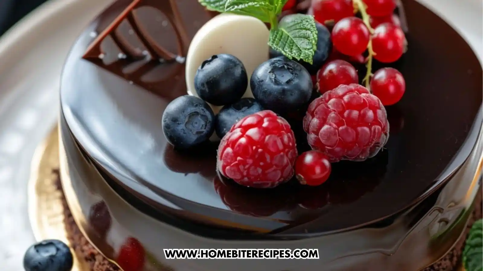 Elegant chocolate mousse cake topped with a shiny ganache layer, fresh berries, and mint, with a slice showing the layered mousse and cake.