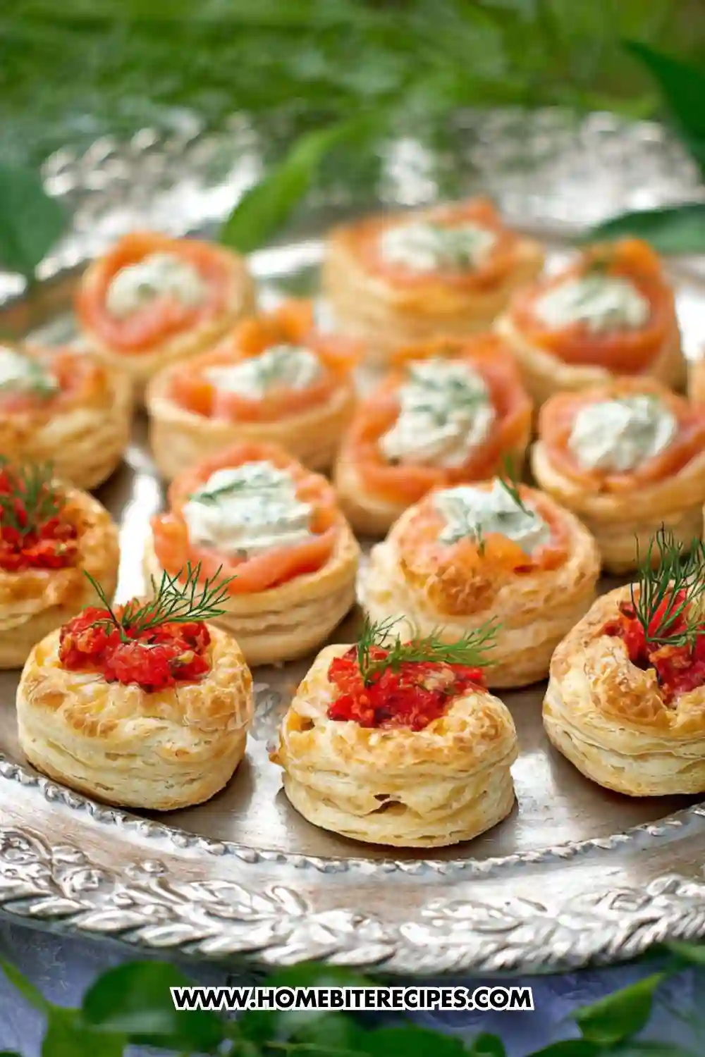 Mini puff pastry vol-au-vents filled with smoked salmon, herbed cream cheese, and red pepper spread, arranged on a silver platter and garnished with fresh dill.