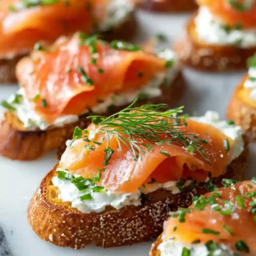 Open-faced crostini topped with creamy herbed cheese, slices of smoked salmon, fresh chives, and dill arranged on a white serving board.