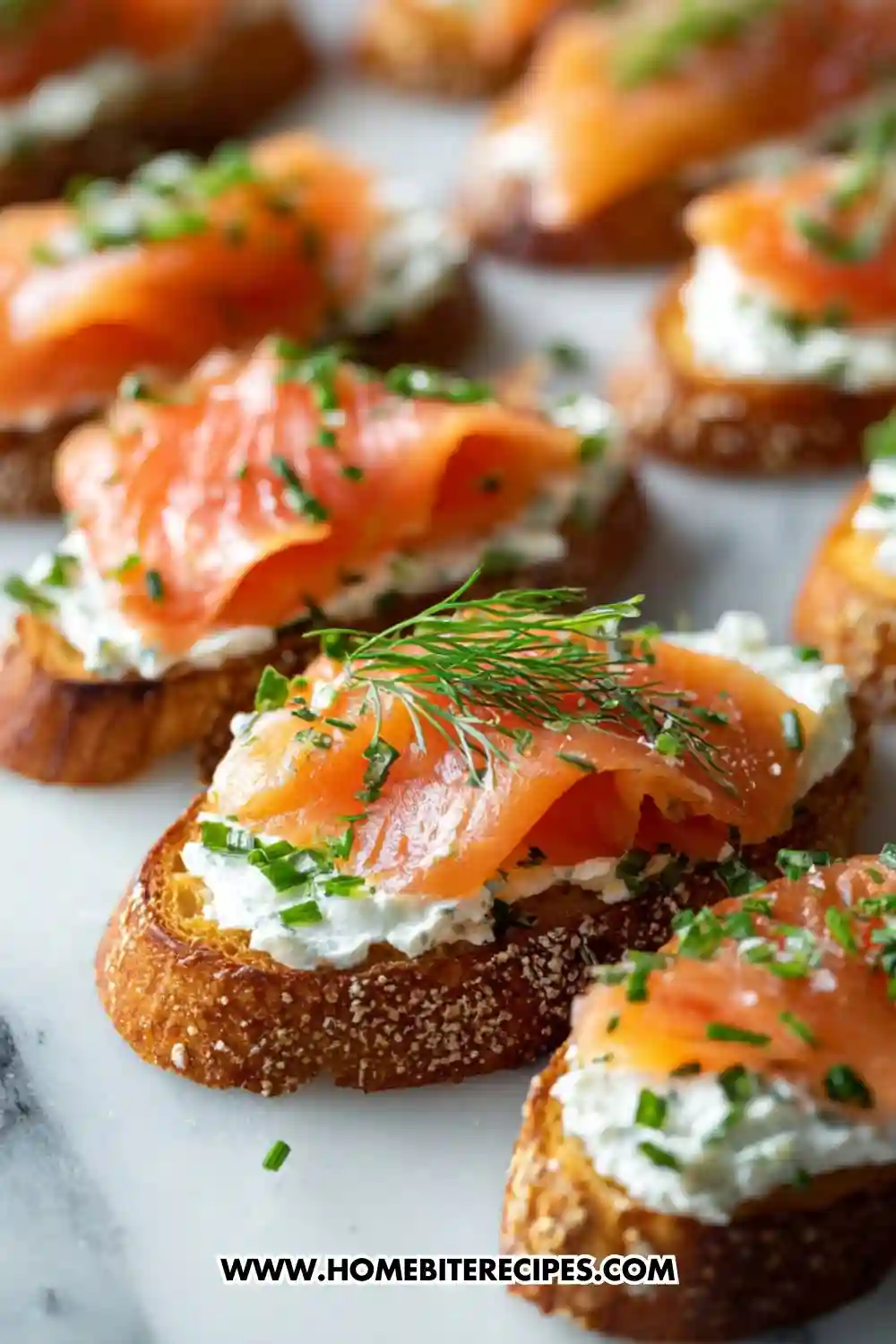 Open-faced crostini topped with creamy herbed cheese, slices of smoked salmon, fresh chives, and dill arranged on a white serving board.