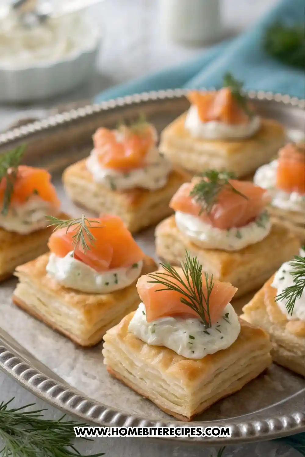 Flaky puff pastry squares topped with smoked salmon, herbed cream cheese, and whipped dill cream, served on a silver platter as elegant party appetizers