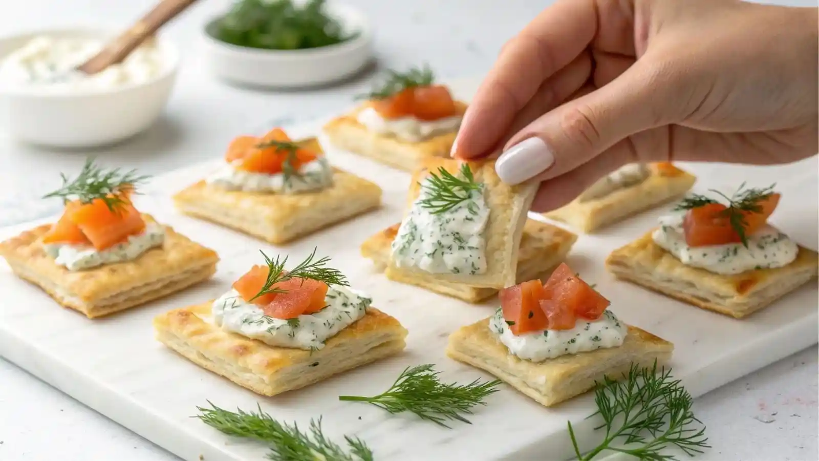 Flaky puff pastry squares topped with smoked salmon, herbed cream cheese, and whipped dill cream, served on a silver platter as elegant party appetizers