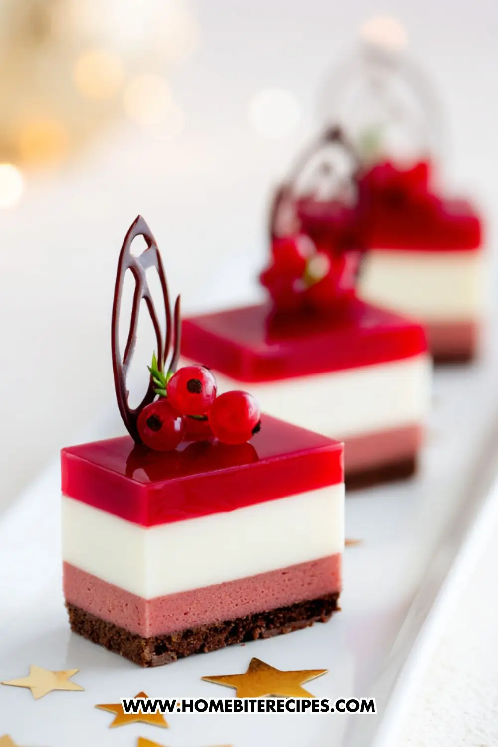 Elegant layered mousse cakes with chocolate base, strawberry mousse, vanilla cream, and glossy red berry jelly topping, decorated with chocolate art and currants