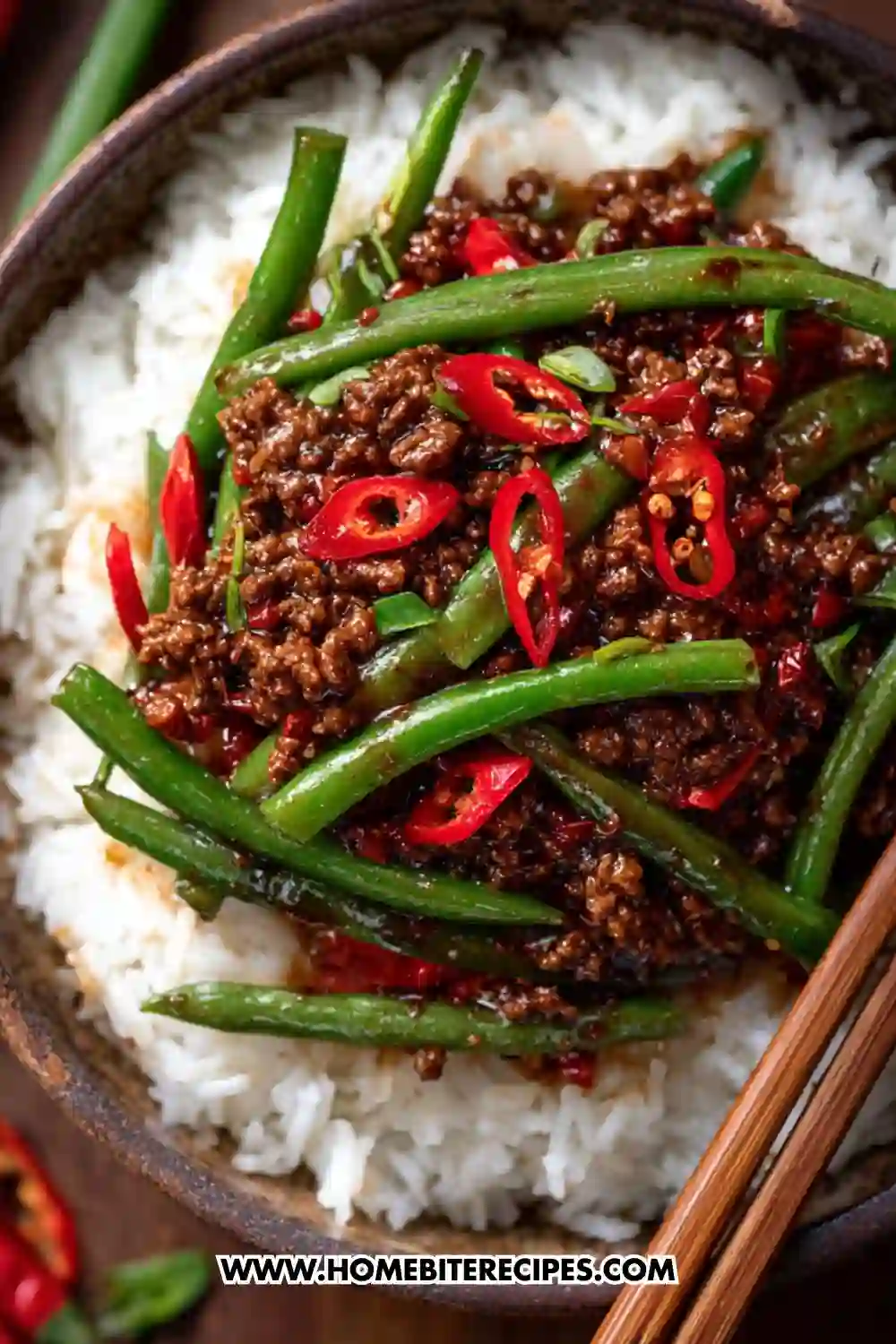 A close-up image of a spicy ground beef stir-fry with green beans and sliced red chili peppers served over fluffy white rice in a bowl with chopsticks.
