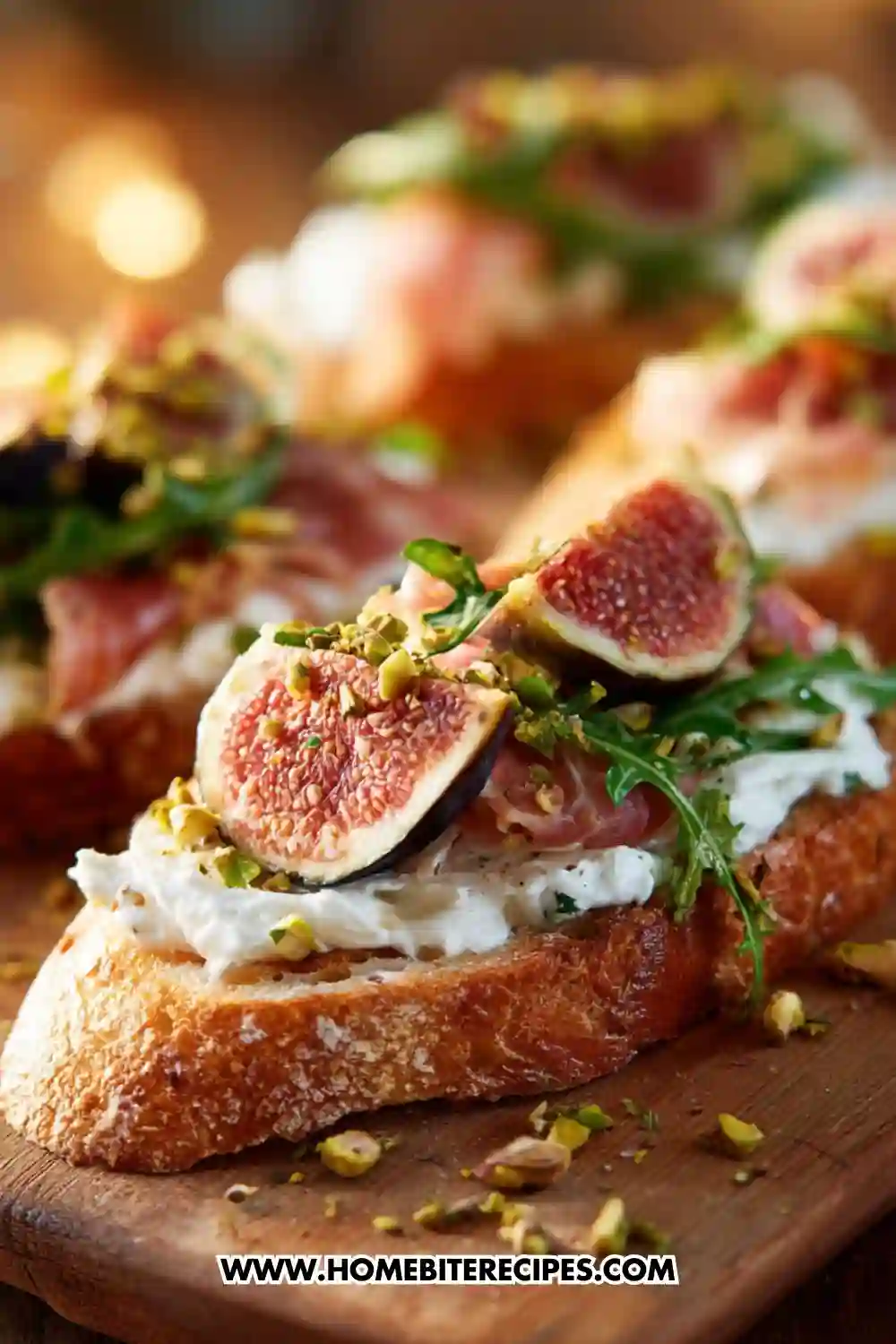 A close-up of gourmet crostini topped with whipped ricotta, prosciutto, fresh figs, arugula, and crushed pistachios on a wooden board.