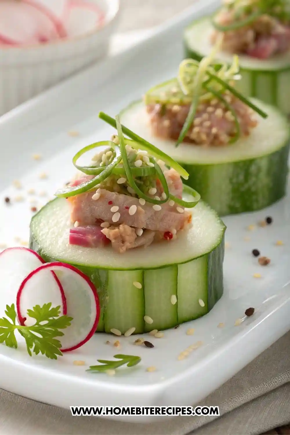 Appetizer made with cucumber slices topped with tuna tartare, sesame seeds, and scallion curls, garnished with radish and cilantro on a white plate.