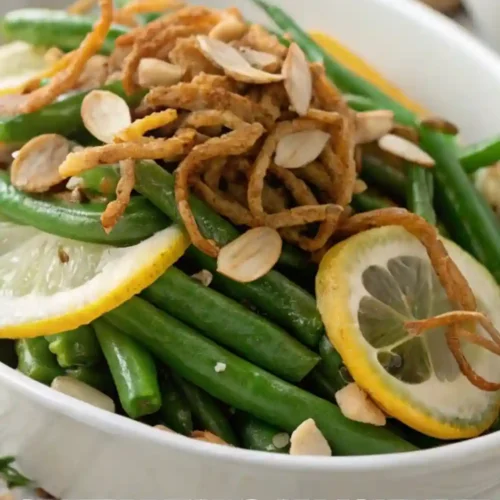 Fresh green beans tossed with toasted almonds and lemon slices, topped with crispy fried onions, served in a white dish.