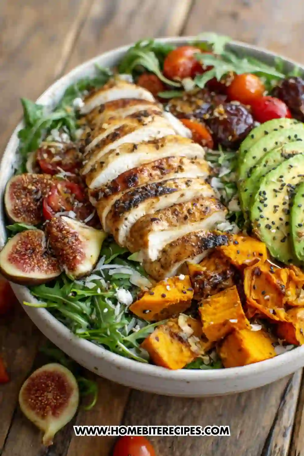 Colorful bowl of grilled chicken salad with avocado, roasted sweet potatoes, fresh figs, arugula, and cherry tomatoes topped with sesame seeds and balsamic drizzle.